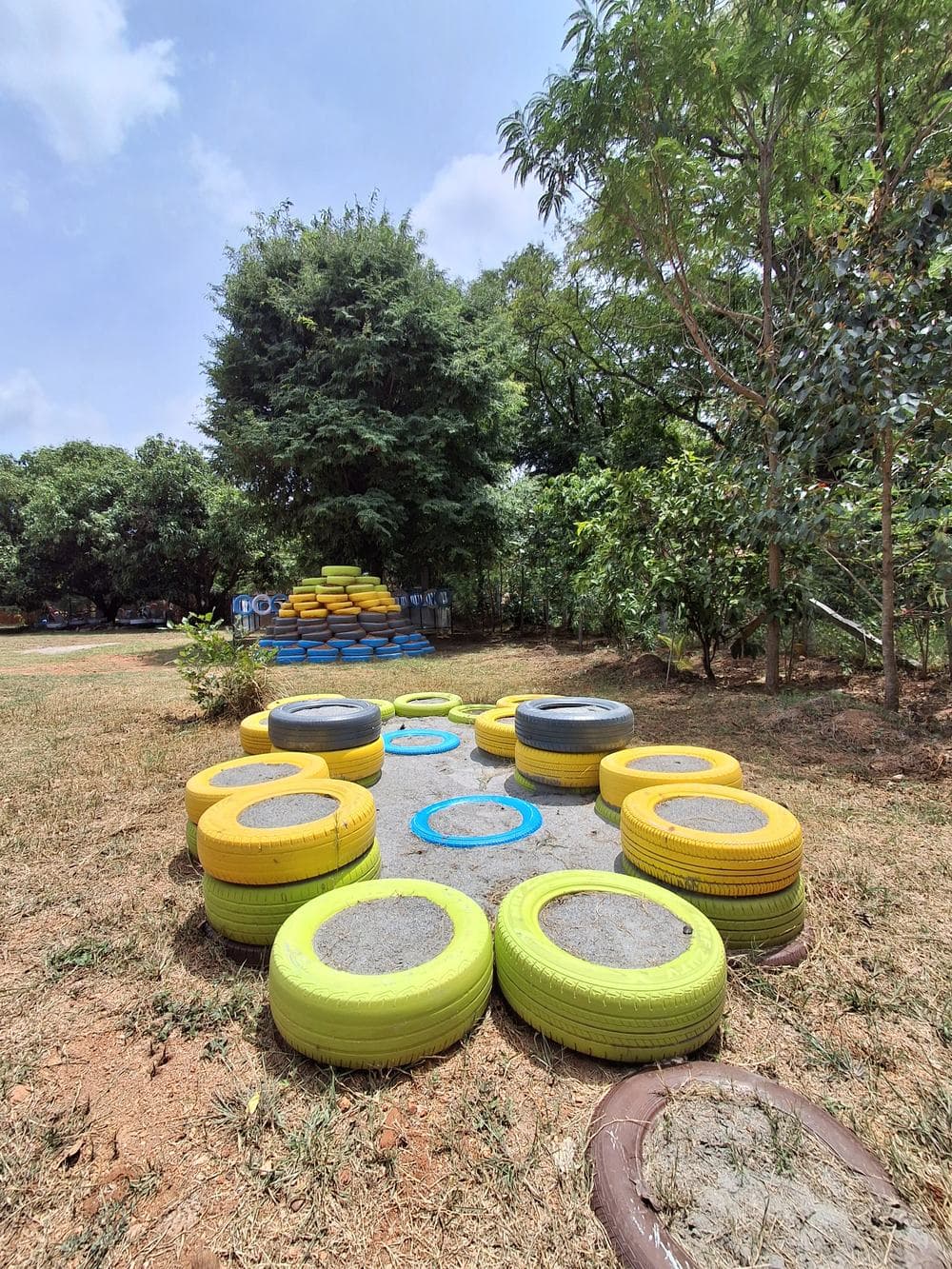 A ring of yellow, green and blue painted tyres set into the grass, with the stacked tyre hill behind it.